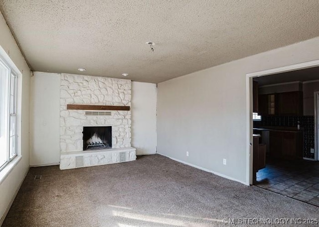 unfurnished living room featuring a textured ceiling, carpet floors, and a stone fireplace