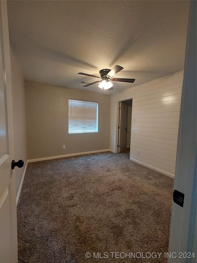 spare room featuring ceiling fan, a textured ceiling, and dark colored carpet