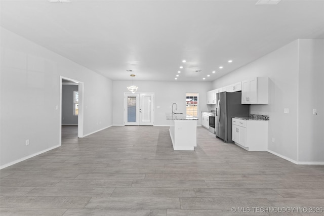 kitchen with sink, appliances with stainless steel finishes, white cabinetry, light stone countertops, and a center island with sink