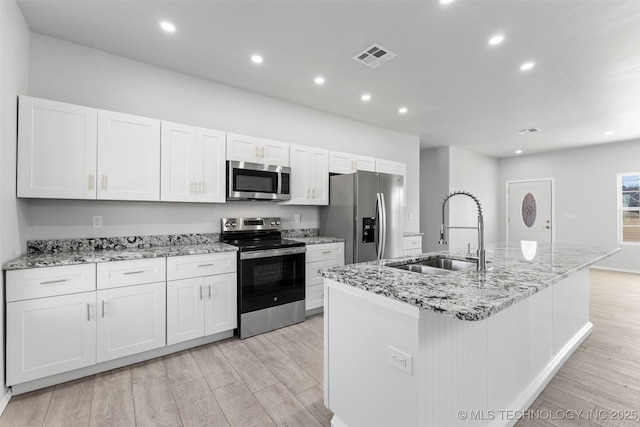 kitchen featuring sink, appliances with stainless steel finishes, white cabinets, a center island with sink, and light wood-type flooring