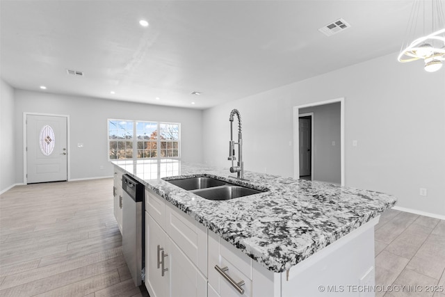 kitchen with sink, dishwasher, white cabinetry, light stone counters, and an island with sink