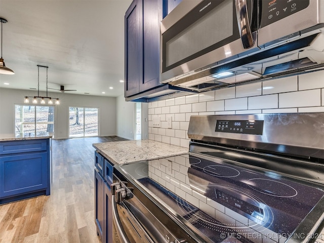 kitchen featuring pendant lighting, decorative backsplash, light stone countertops, blue cabinetry, and appliances with stainless steel finishes