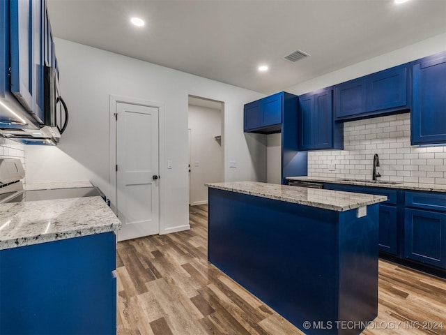 kitchen featuring stove, sink, light stone countertops, blue cabinetry, and a kitchen island