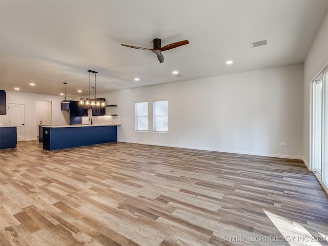 unfurnished living room featuring ceiling fan with notable chandelier, light hardwood / wood-style floors, and sink