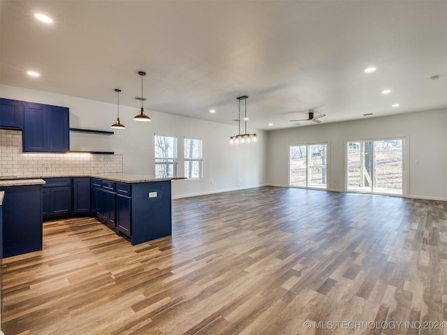 kitchen with blue cabinetry, tasteful backsplash, light stone counters, light hardwood / wood-style flooring, and decorative light fixtures