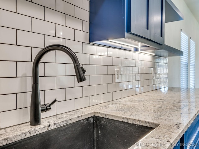 kitchen featuring light stone counters, sink, blue cabinets, and backsplash