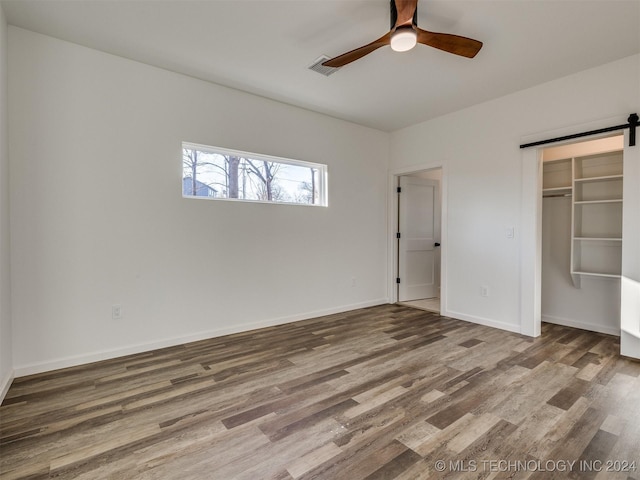 unfurnished bedroom featuring ceiling fan, a barn door, wood-type flooring, and a closet