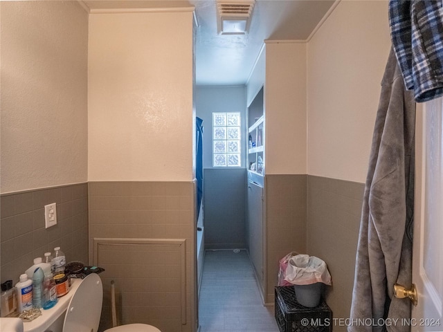 bathroom featuring toilet, tile walls, and ornamental molding