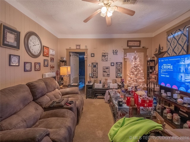 carpeted living room with a textured ceiling, ceiling fan, and wood walls