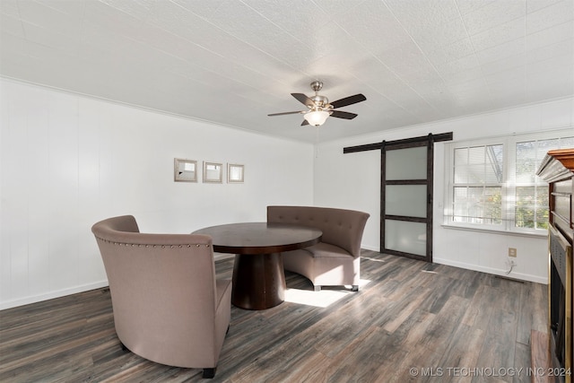 unfurnished dining area featuring a barn door, ceiling fan, dark wood-type flooring, and ornamental molding