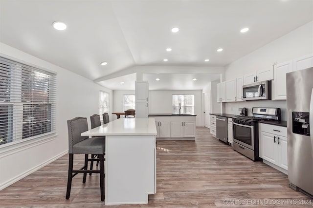 kitchen with a kitchen island, light hardwood / wood-style floors, a breakfast bar, white cabinets, and appliances with stainless steel finishes