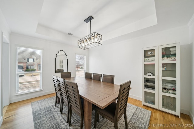 dining room featuring light hardwood / wood-style floors, ornamental molding, and a raised ceiling