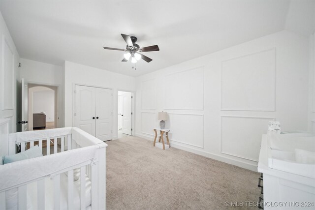 bedroom featuring ceiling fan, a closet, light carpet, and a crib