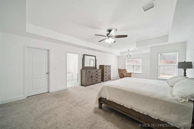 bedroom featuring ceiling fan, ensuite bathroom, and a raised ceiling