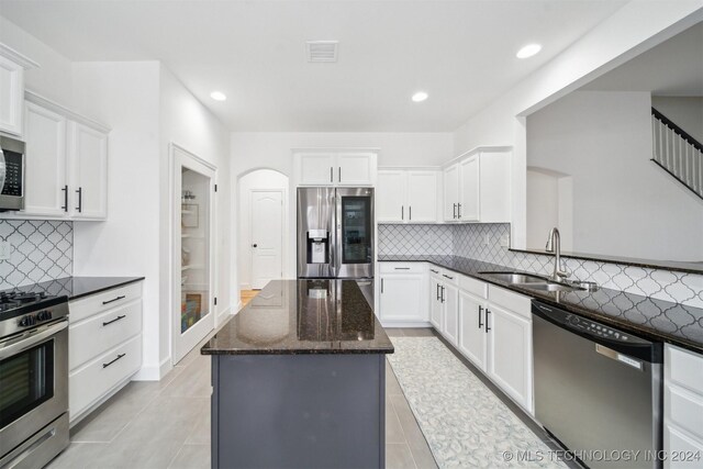 kitchen with white cabinets, stainless steel appliances, dark stone counters, sink, and backsplash