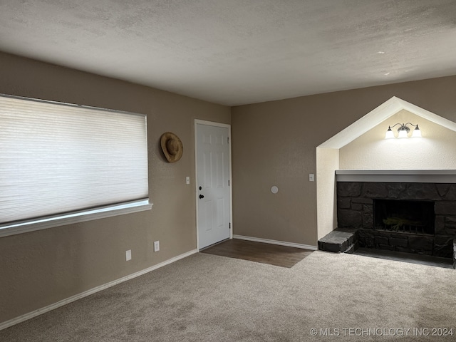 unfurnished living room featuring a textured ceiling, carpet floors, and a stone fireplace