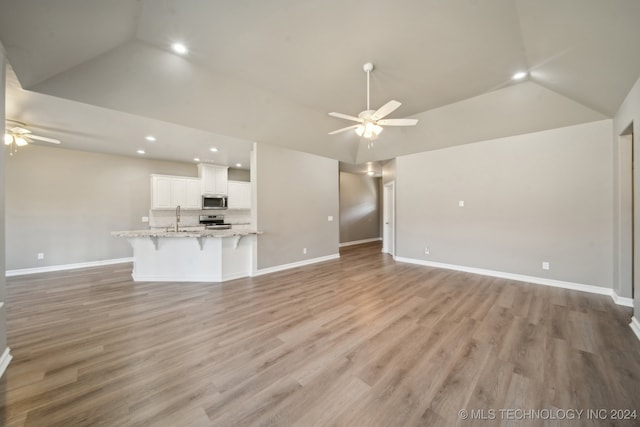 unfurnished living room featuring lofted ceiling, light wood-style flooring, a ceiling fan, and a sink