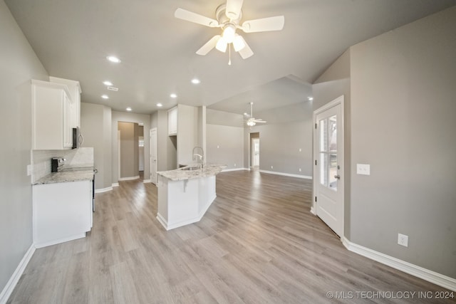 kitchen featuring open floor plan, decorative backsplash, light wood-style flooring, white cabinetry, and a sink