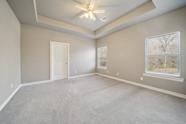 carpeted empty room with a tray ceiling, baseboards, visible vents, and ceiling fan