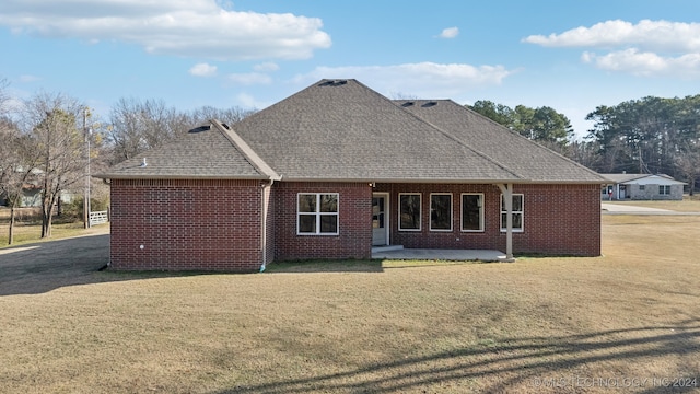 rear view of house featuring brick siding, roof with shingles, and a lawn