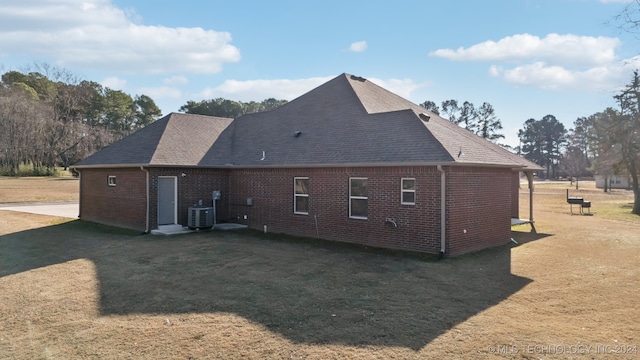 back of house featuring cooling unit, a lawn, brick siding, and a shingled roof