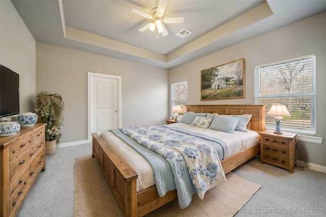 bedroom featuring light colored carpet, a raised ceiling, baseboards, and visible vents