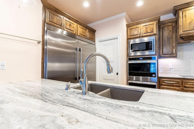 kitchen featuring built in appliances, sink, crown molding, and light stone countertops