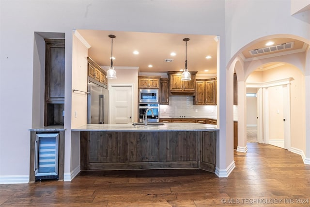 kitchen with beverage cooler, built in appliances, decorative light fixtures, and kitchen peninsula