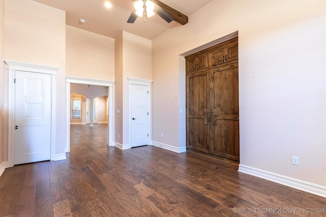 unfurnished bedroom with dark hardwood / wood-style flooring, beam ceiling, ceiling fan, and a towering ceiling