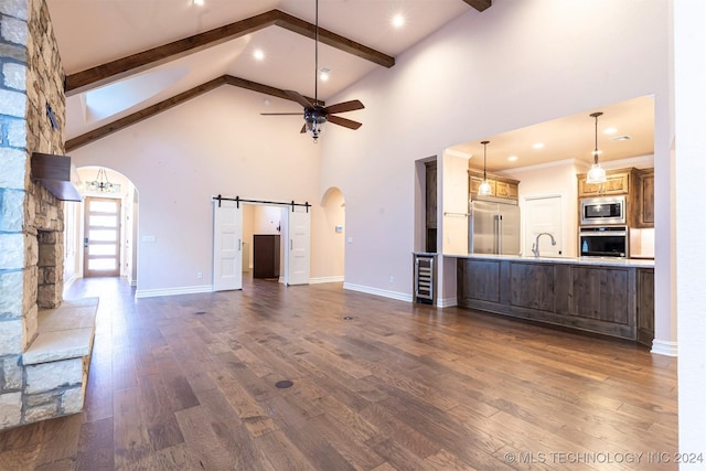 unfurnished living room featuring dark wood-type flooring, sink, beam ceiling, ceiling fan, and a barn door