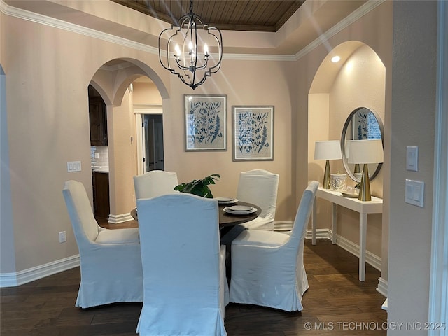 dining space featuring dark wood-type flooring, a tray ceiling, a chandelier, and crown molding