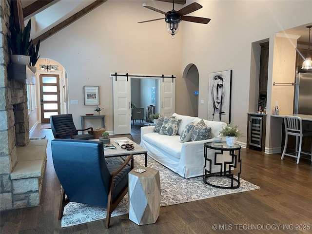 living room with wine cooler, dark hardwood / wood-style flooring, beamed ceiling, ceiling fan, and a barn door