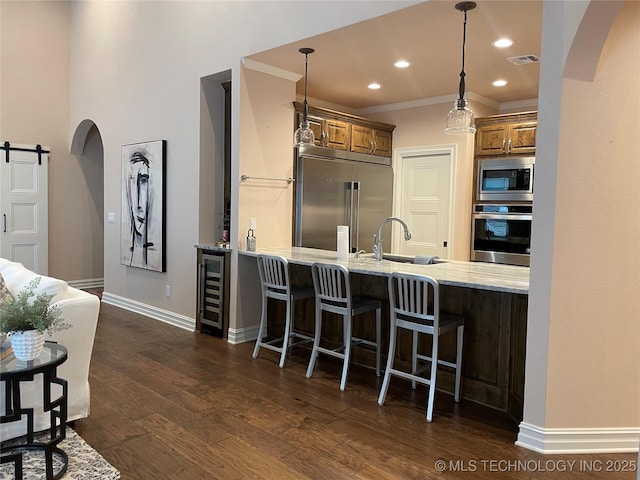 kitchen featuring sink, built in appliances, kitchen peninsula, a kitchen bar, and a barn door