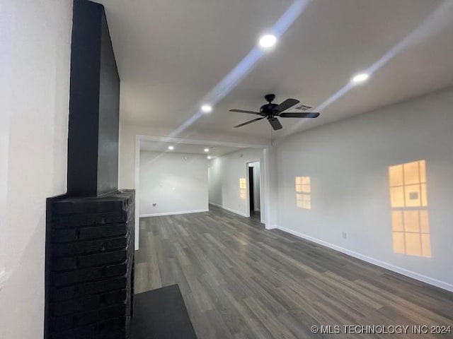 unfurnished living room featuring dark hardwood / wood-style floors, ceiling fan, and a wood stove