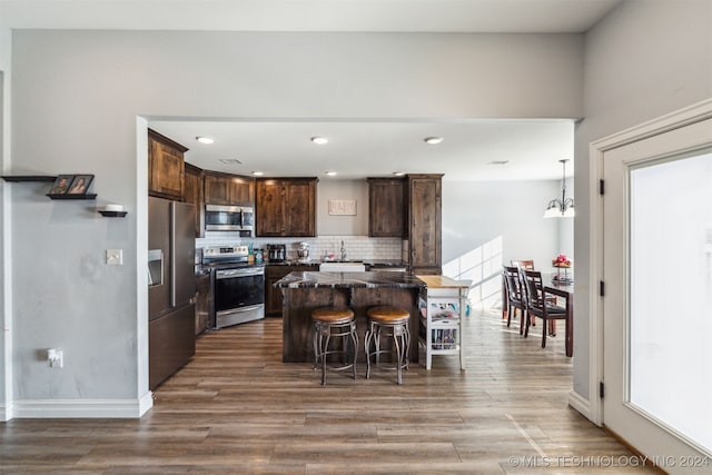 kitchen featuring dark brown cabinetry, a center island, stainless steel appliances, backsplash, and a breakfast bar area