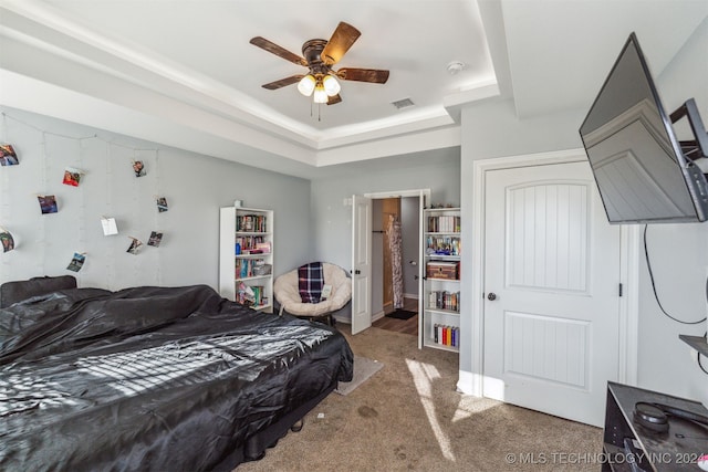 carpeted bedroom with ceiling fan and a raised ceiling