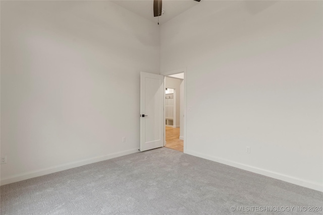 empty room featuring ceiling fan, a towering ceiling, and light colored carpet