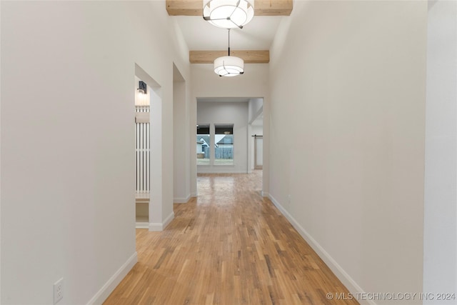 hall featuring beamed ceiling, light wood-type flooring, and a towering ceiling