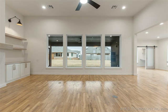 unfurnished living room featuring a barn door, ceiling fan, plenty of natural light, and light hardwood / wood-style flooring