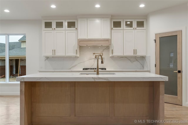 kitchen with white cabinets, a center island with sink, tasteful backsplash, and light stone countertops