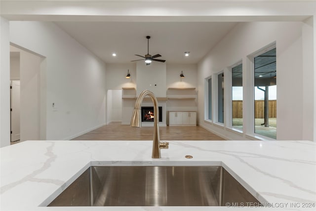 kitchen with hardwood / wood-style flooring, light stone counters, ceiling fan, and sink