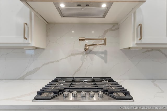 room details with decorative backsplash, white cabinets, light stone counters, and stainless steel gas stovetop