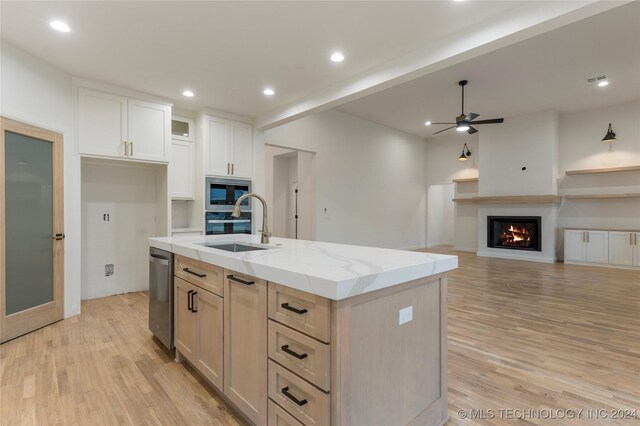 kitchen with light stone countertops, stainless steel appliances, ceiling fan, a center island with sink, and white cabinetry