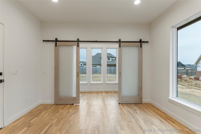 spare room with a barn door, french doors, and light hardwood / wood-style floors