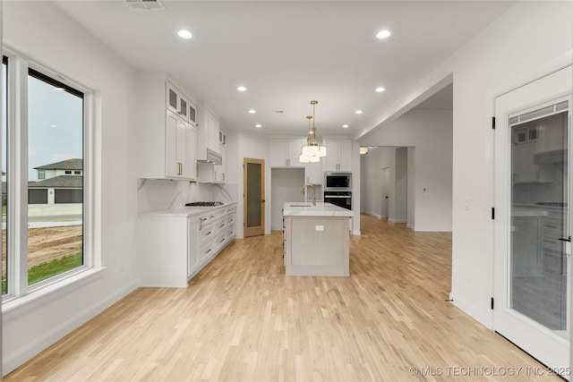 kitchen featuring light wood finished floors, light countertops, a sink, stainless steel microwave, and wall oven