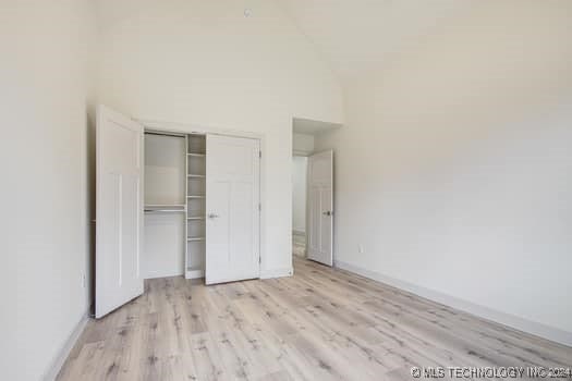 unfurnished bedroom with a closet, high vaulted ceiling, and light wood-type flooring