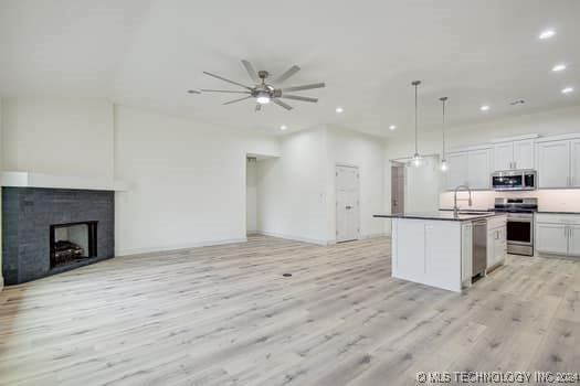 kitchen featuring decorative light fixtures, stainless steel appliances, white cabinetry, and a center island with sink