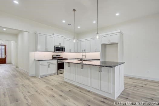 kitchen with sink, pendant lighting, a kitchen island with sink, white cabinets, and appliances with stainless steel finishes