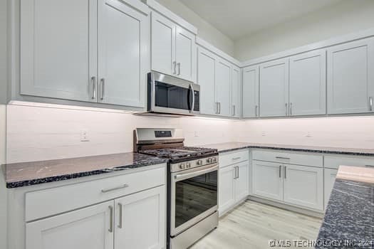 kitchen featuring dark stone countertops, white cabinetry, light hardwood / wood-style flooring, and appliances with stainless steel finishes