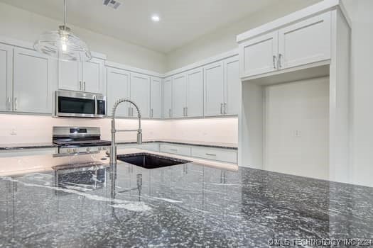 kitchen featuring stove, sink, decorative light fixtures, dark stone countertops, and white cabinets